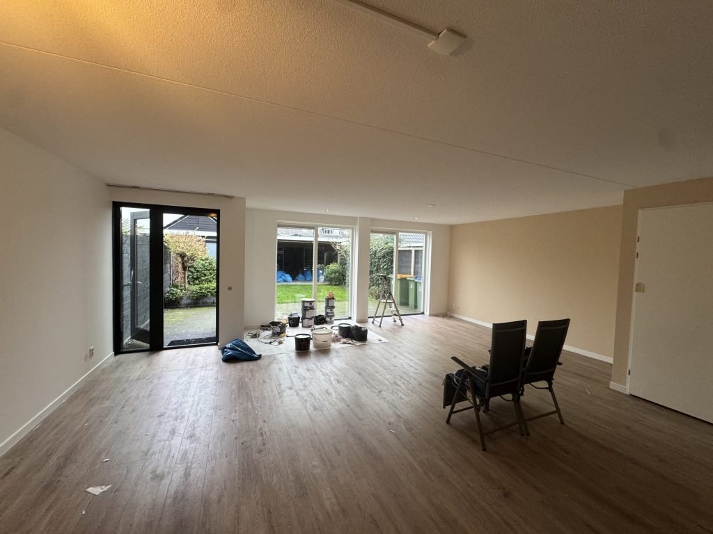 Leeggeruimde woonkamer van een rijtjeshuis met tuindeuren, klaar om opnieuw behangen te worden